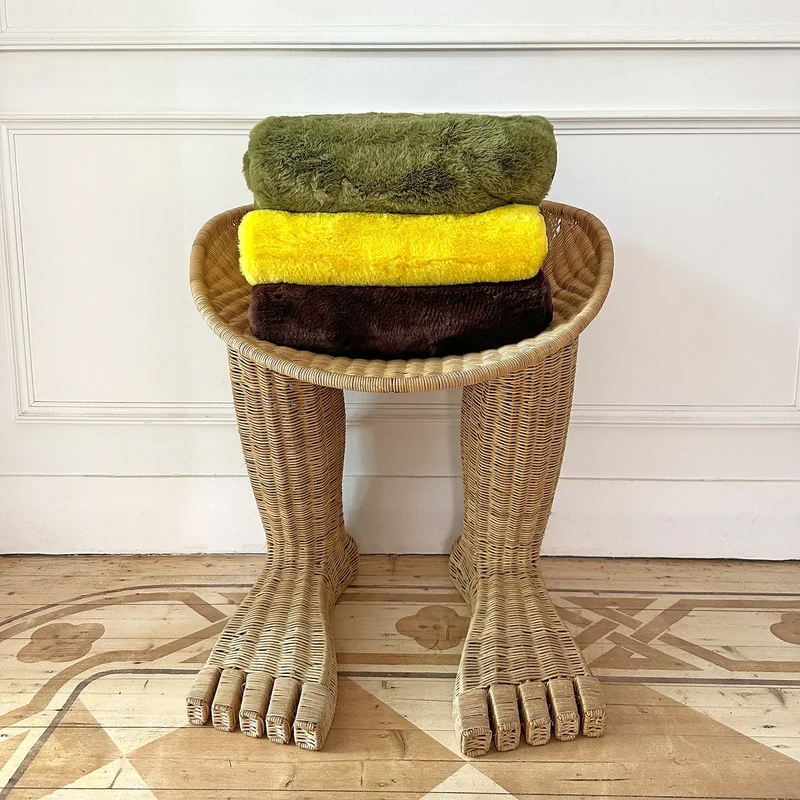 Stack of green, yellow, and brown dog blankets on a unique wicker chair with foot-shaped legs
