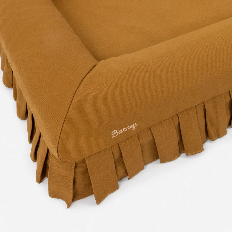 Nostalgia Cover in Toffee: close-up of a corner, with "Barney" embroidered in cream script above the pleated skirt.