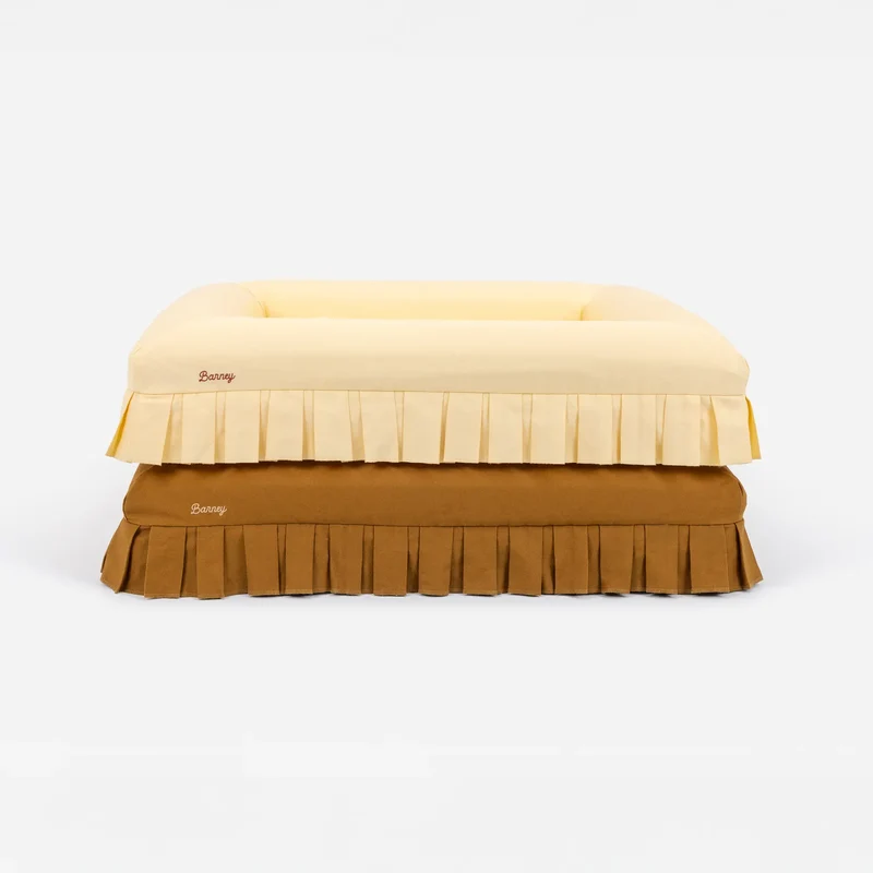 Nostalgia Cover in Buttercream and Toffee: two beds stacked, pale yellow on toffee, each with pleats and a "Barney" logo.