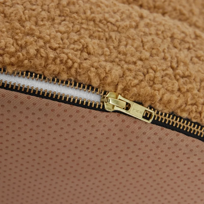 Close-up of a tan dog bed with a visible gold zipper detail