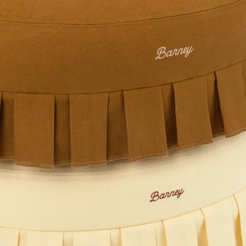 Nostalgia Cover Curl in Toffee and Buttercream: close-up of both pleated skirts and their embroidered script "Barney" logos.