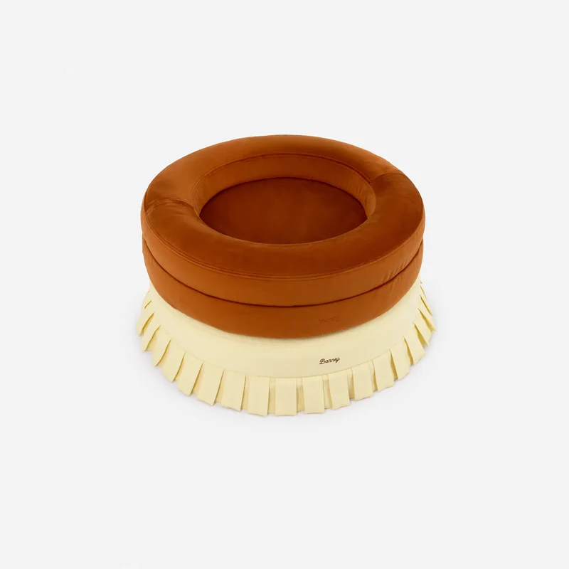 Velvet Cover Curl in Sunset on a BarneyCurl, set on a pale yellow round bed with a pleated skirt.