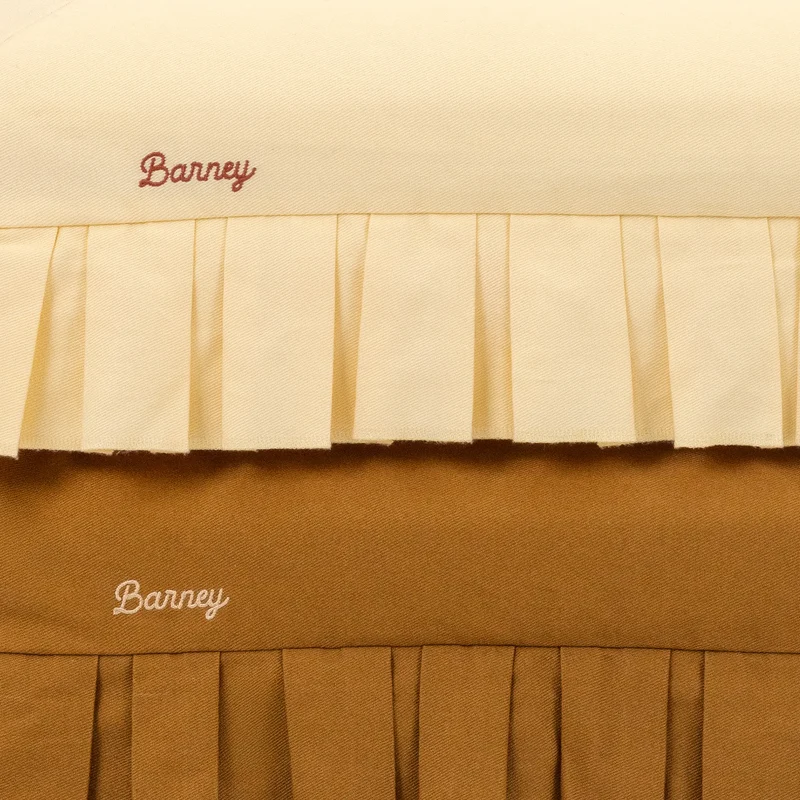 Nostalgia Cover in Buttercream and Toffee: close-up of both pleated skirts and their embroidered script "Barney" logos.