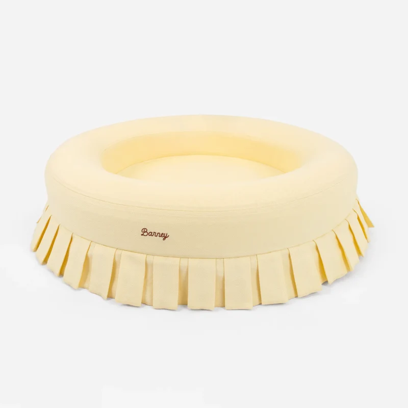 Nostalgia Cover Curl in Buttercream: the round pale yellow bed from a low angle, with pleated skirt and script "Barney" logo.